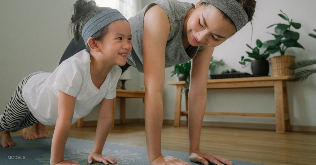 A mother and her child (models) doing yoga together in the kitchen looking happy.